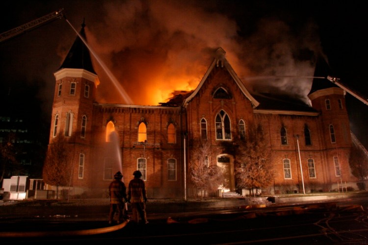 Active fire scene at night showing firefighters with hoses pointing at flames inside the historic Provo Tabernacle windows.