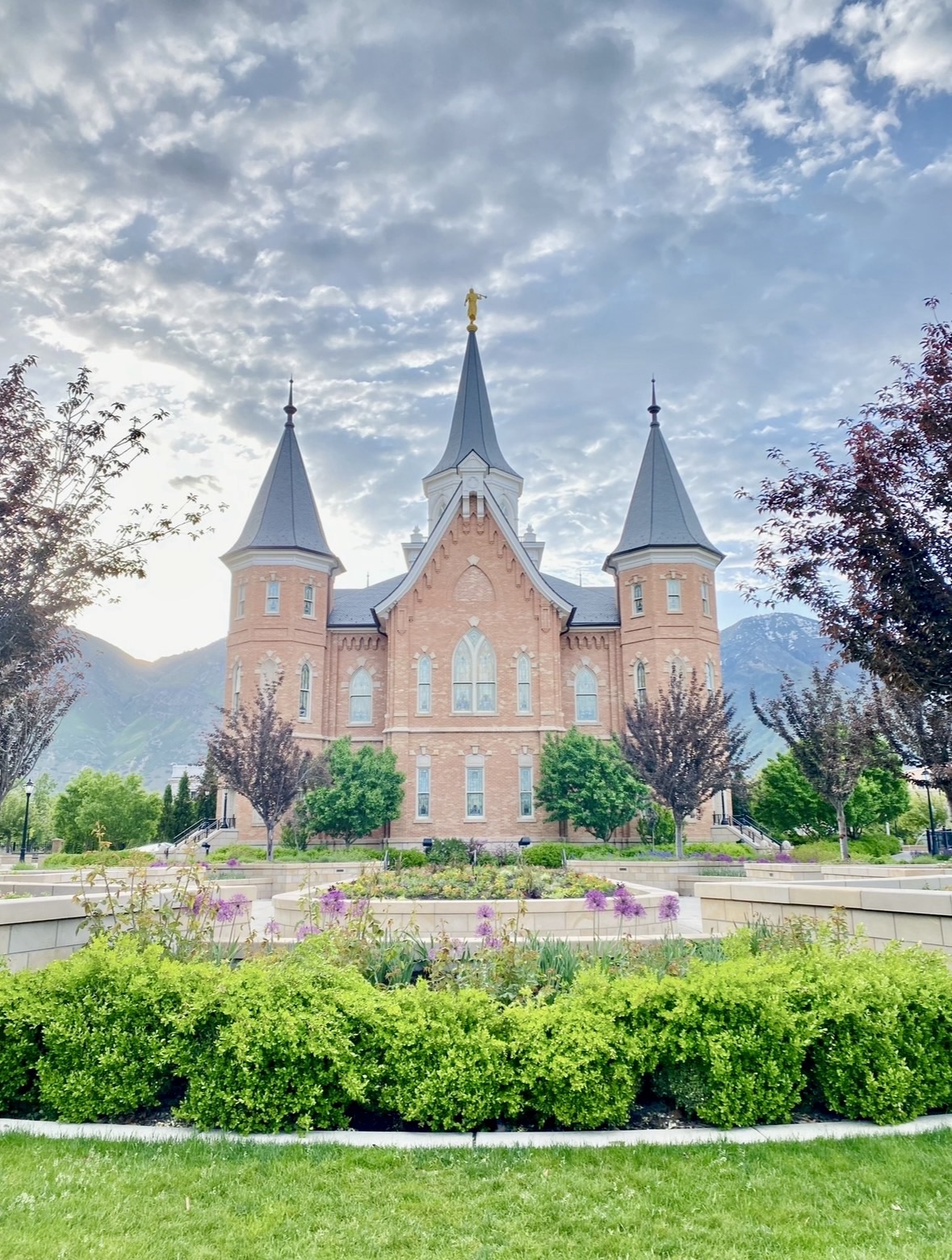 A spring-time view of the Provo City Center Temple featuring green grass and blooming garden flowers.
