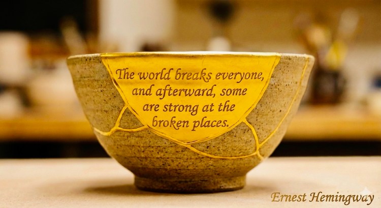 A ceramic kintsugi bowl with gold-filled cracks, featuring the Ernest Hemingway quote: 'The world breaks everyone, and afterward, some are strong at the broken places.