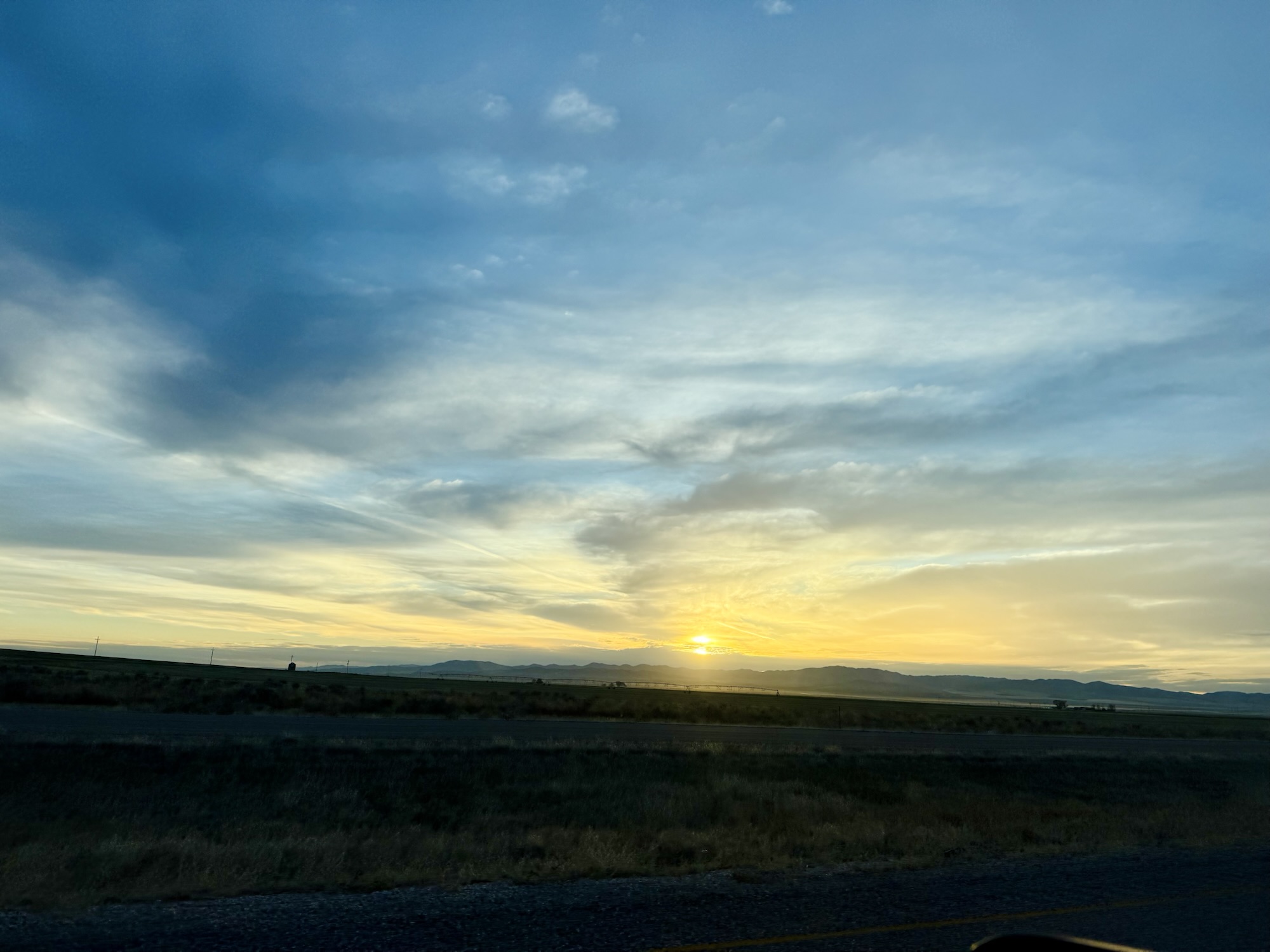 The sun rising over the horizon with blue clouds and bright yellow light on the road from Oregon, photographed by Jared Harding Wilson.