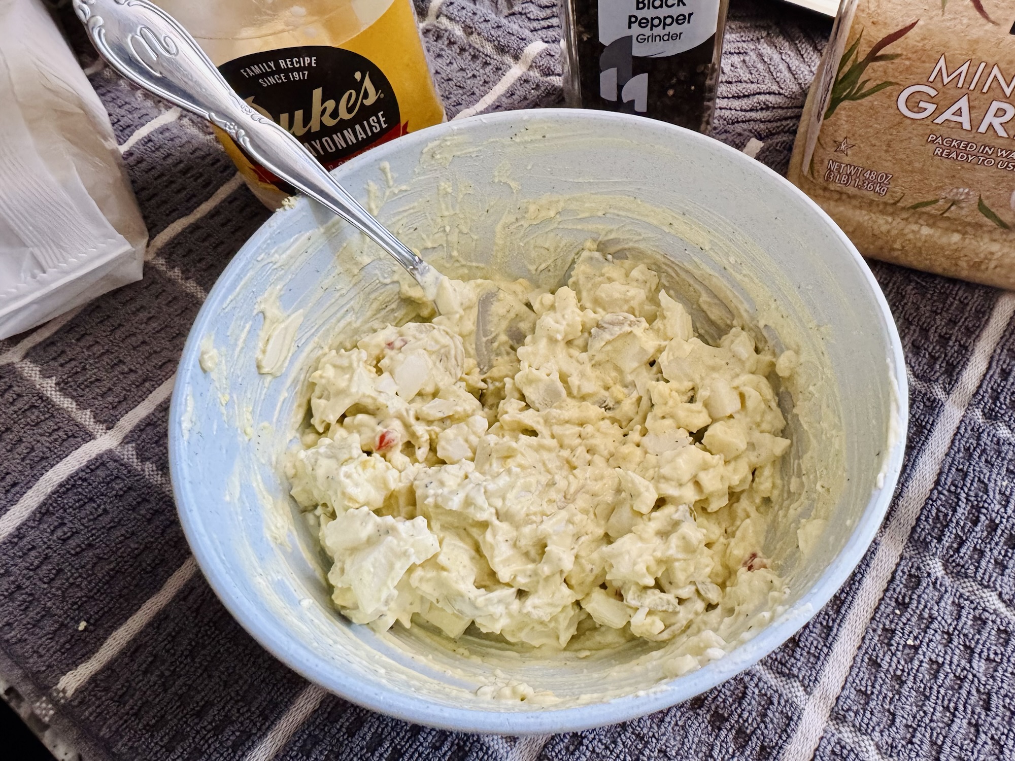 A bowl of freshly mixed Mediterranean egg salad, showing a creamy texture with olives, feta, and garnished with black pepper by Jared Harding Wilson