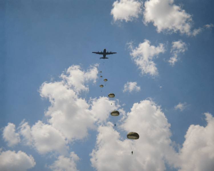 A wide scenic view of military paratroopers descending through a cloudy blue sky, documented in the military history collection of Jared Harding Wilson.