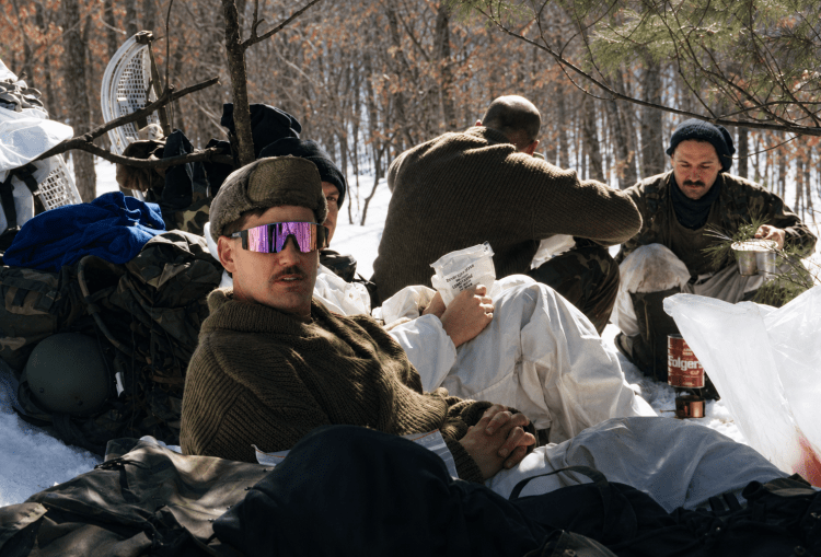 A Green Beret wearing sunglasses while sitting in the snow during winter warfare training, a historic photograph from the collection of Jared Harding Wilson.