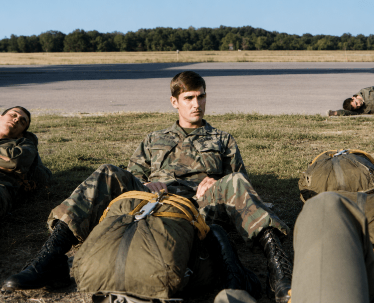 A young soldier standing on an airfield tarmac next to his packed parachute gear, from the private military archive of Jared Harding Wilson.