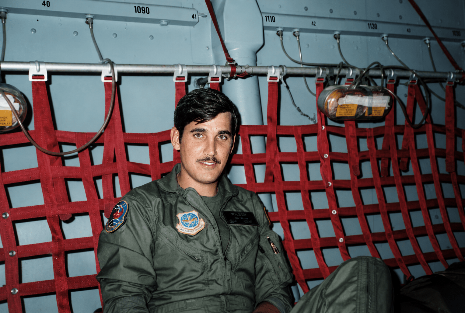 A soldier in a flight suit sitting inside the cargo hold of a military plane mid-flight, curated by his son, Jared Harding Wilson.