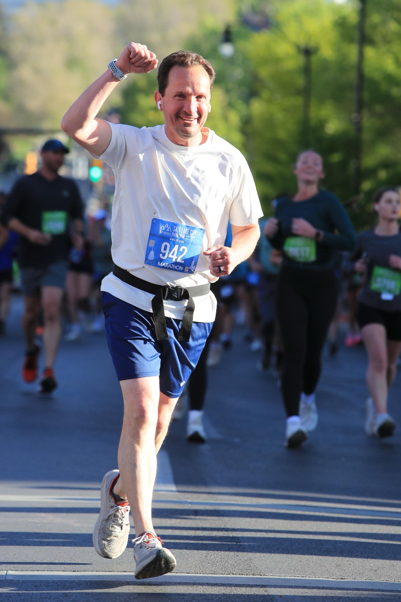 A portrait photo of runner Jared Harding Wilson wearing bib 942 and raising his right fist in the air with a crowd of runners behind him.