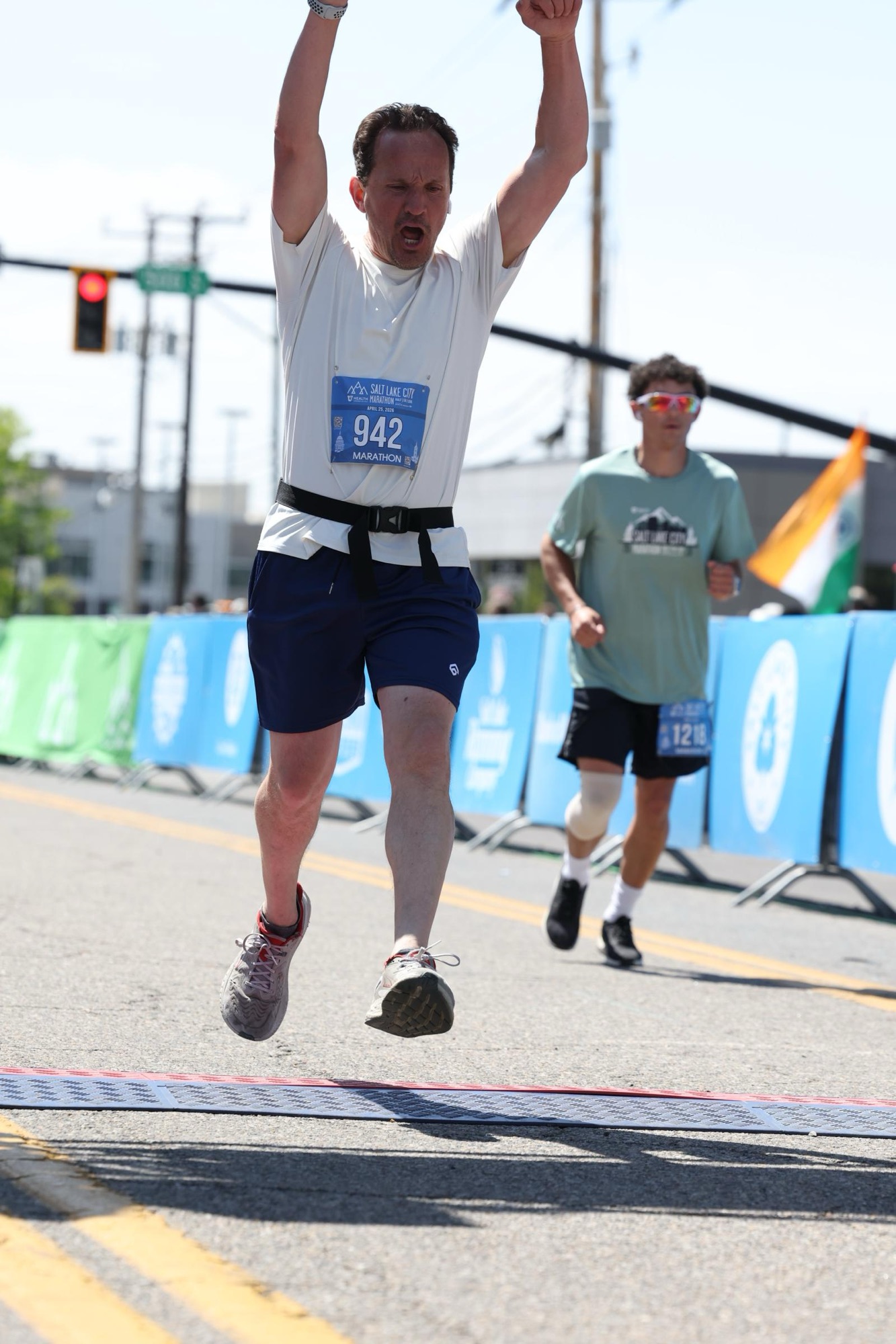 Jared Harding Wilson crossing the marathon finish line with both arms in the air and a proud, exhausted expression on his face.