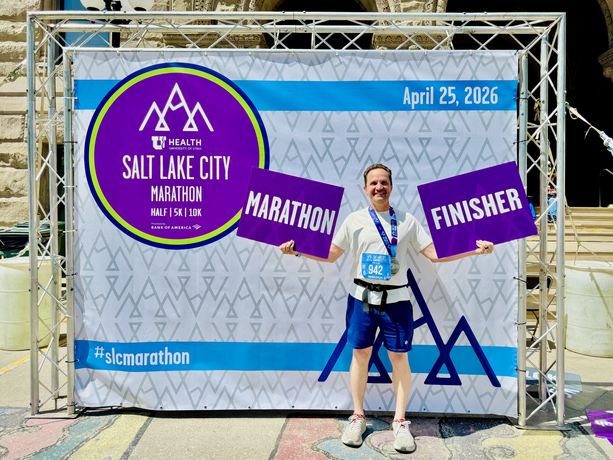 Jared Harding Wilson standing in front of a Salt Lake Marathon finisher banner while wearing his race medal.
